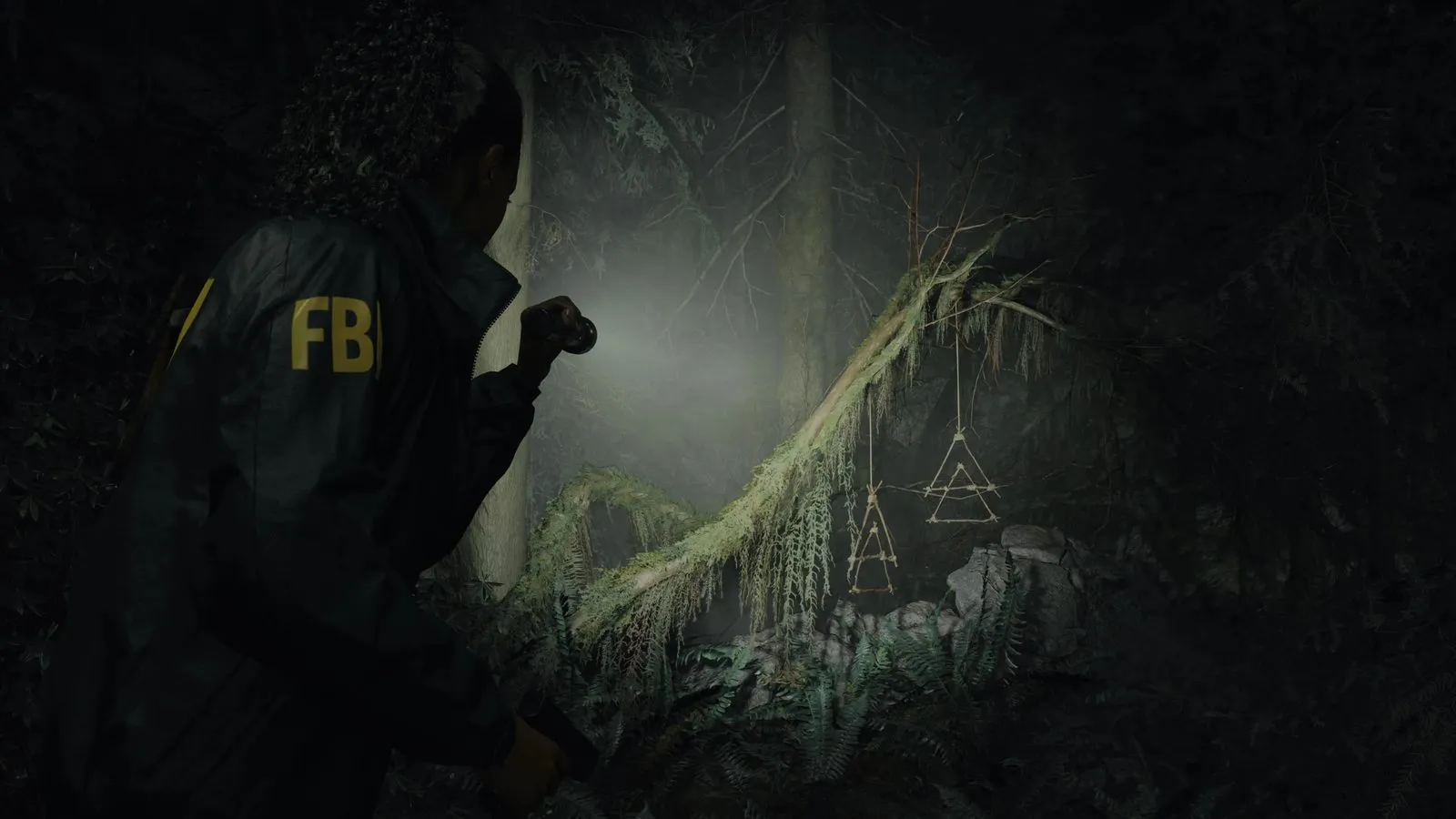 Saga Anderson ilumina con su linterna unos símbolos de ramitas colgados en el bosque