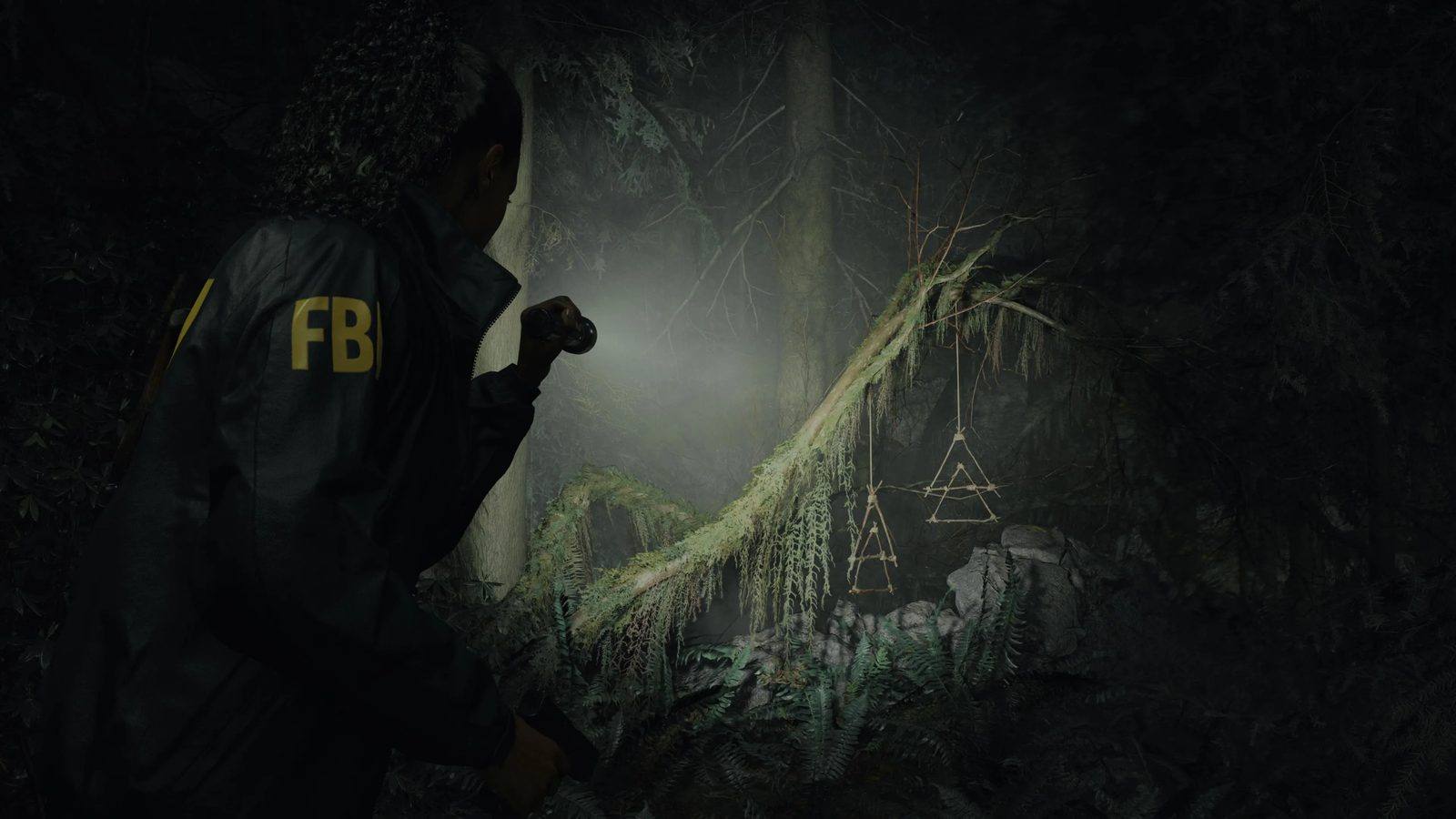 Saga Anderson, con chaqueta del FBI, ilumina con su linterna unos símbolos de ramitas que cuelgan de un árbol caído en un bosque de noche