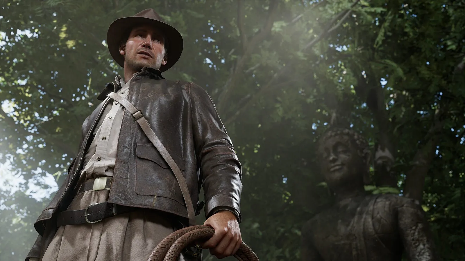 Indiana Jones con el látigo enrollado, visto desde abajo, junto a una estatua entre la vegetación