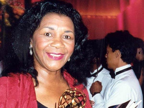 Retrato de la actriz Mary Alice sonriendo, con un chal rojo, en una fiesta de los premios Emmy con otras personas al fondo