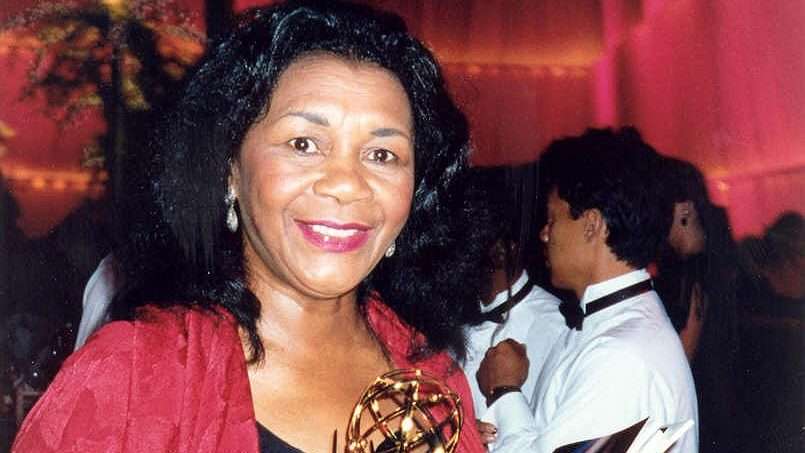 Retrato de la actriz Mary Alice sonriendo, con un chal rojo, en una fiesta de los premios Emmy con otras personas al fondo