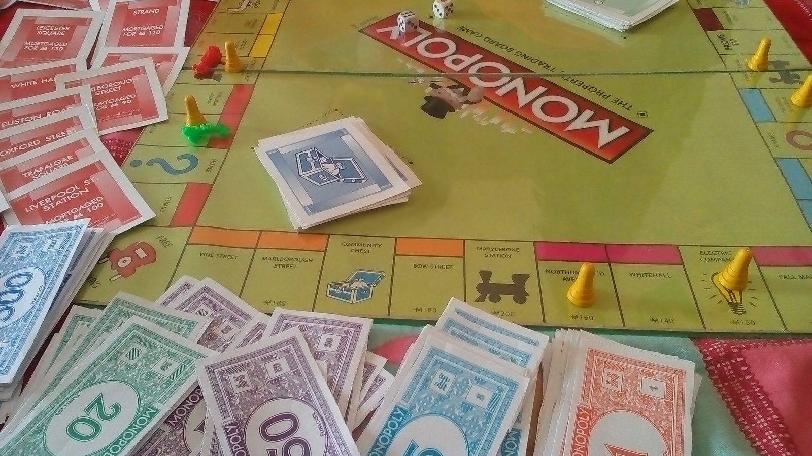 Una partida de Monopoly en curso con tablero, dados, fichas amarillas, billetes de colores y tarjetas de propiedad sobre una mesa