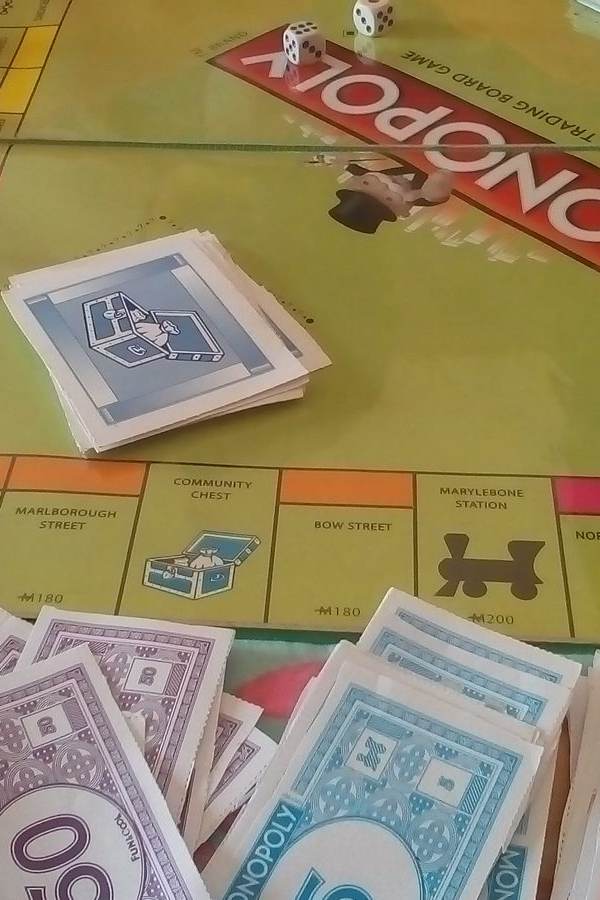 Una partida de Monopoly en curso con tablero, dados, fichas amarillas, billetes de colores y tarjetas de propiedad sobre una mesa