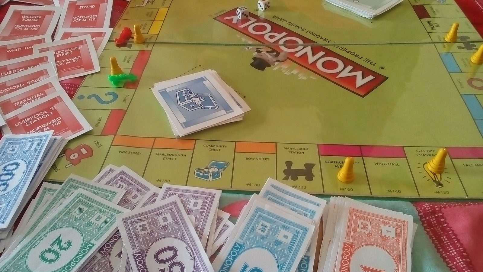 Una partida de Monopoly en curso con tablero, dados, fichas amarillas, billetes de colores y tarjetas de propiedad sobre una mesa
