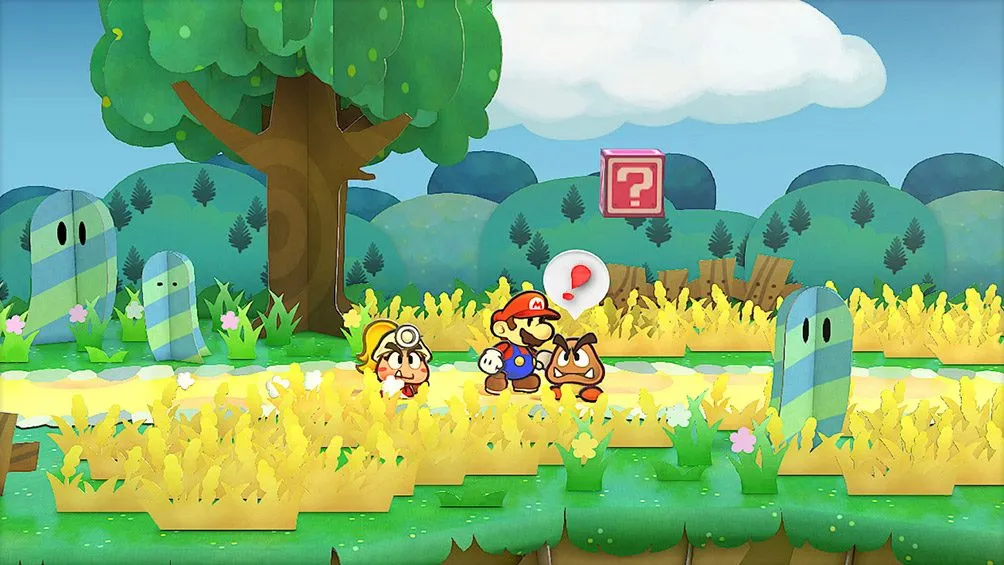 Mario camina junto a Goombella, una Goomba con casco de minero, y otro Goomba; sobre ellos aparece un globo con un signo de exclamación, entre hierba amarilla y árboles de papel, con un bloque de interrogación al fondo