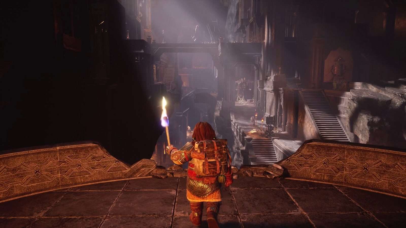 Un enano visto de espaldas, con una mochila grande y una antorcha encendida, mira una enorme sala de la mina de Moria con escaleras y columnas