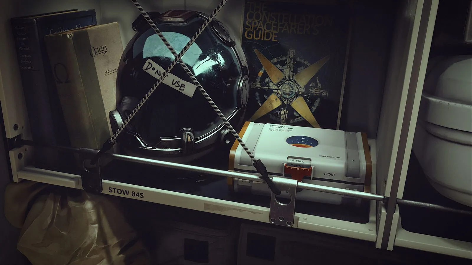 Un casco de traje espacial con una etiqueta de cinta que dice 'Don't use', sujeto con cuerdas junto a libros, un póster y una caja blanca de Constellation en un estante