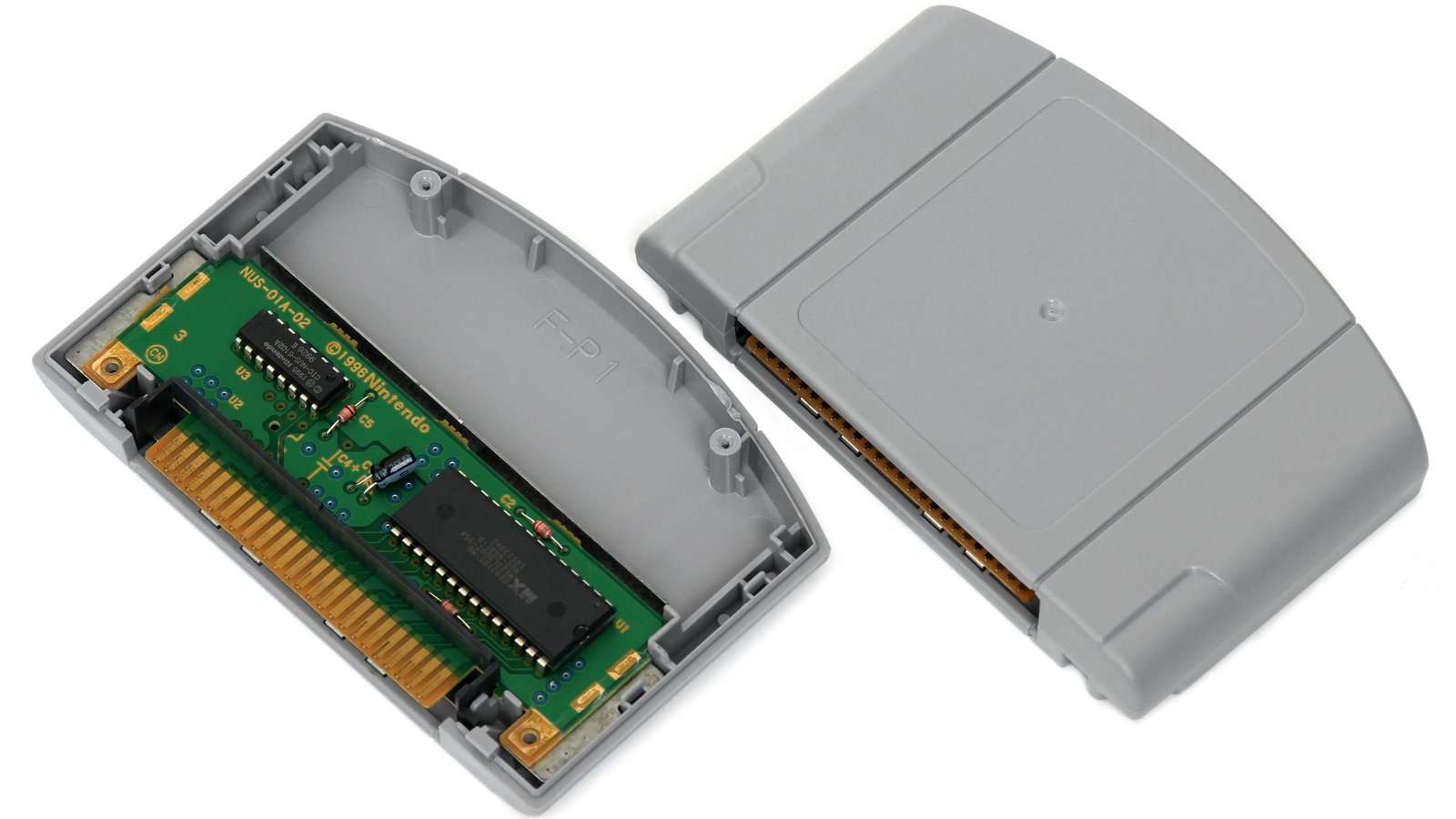 Cartucho gris de Nintendo 64, abierto a la izquierda con la placa verde a la vista y cerrado a la derecha, sobre fondo blanco y sin etiqueta de ningún juego