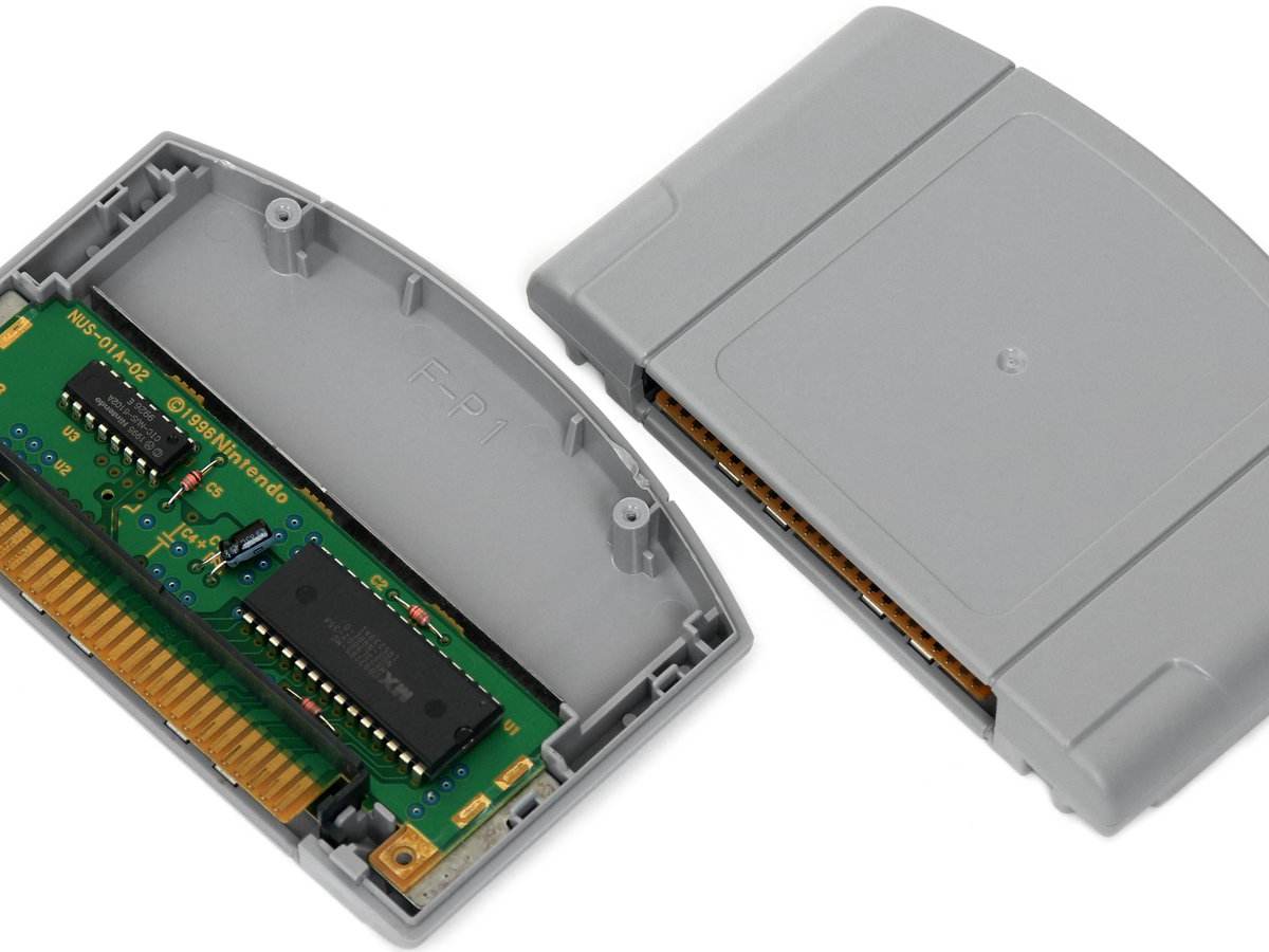 Cartucho gris de Nintendo 64, abierto a la izquierda con la placa verde a la vista y cerrado a la derecha, sobre fondo blanco y sin etiqueta de ningún juego
