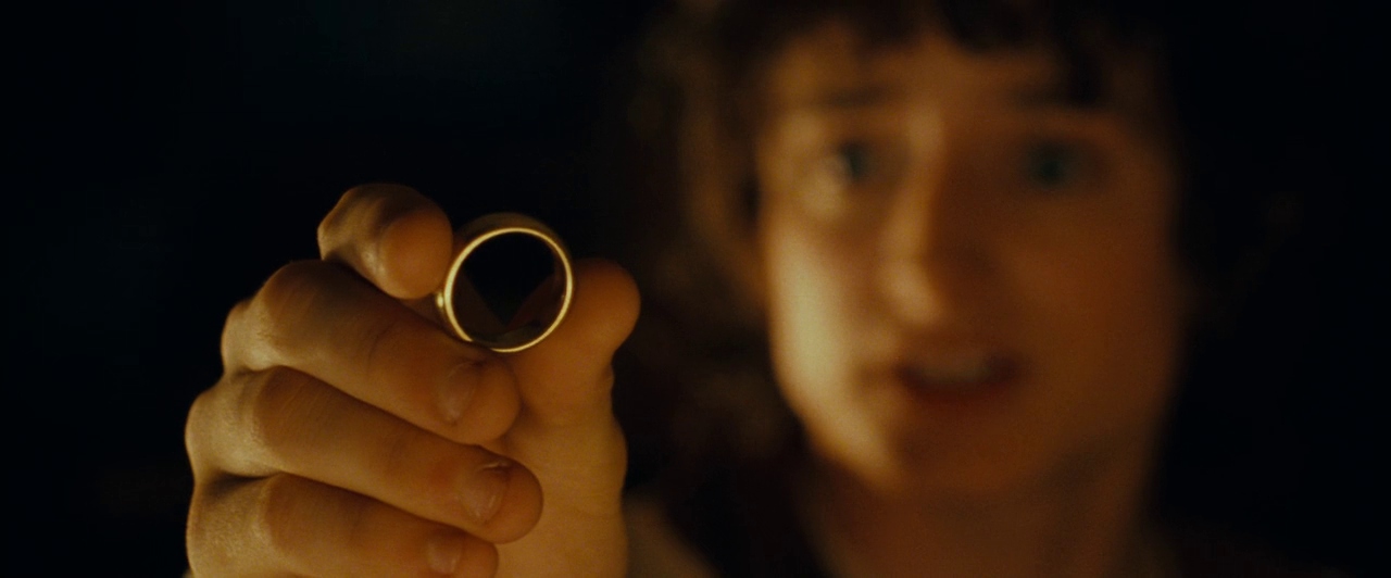 Frodo, desenfocado en el fondo, sostiene el Anillo Único en La comunidad del anillo de Peter Jackson.