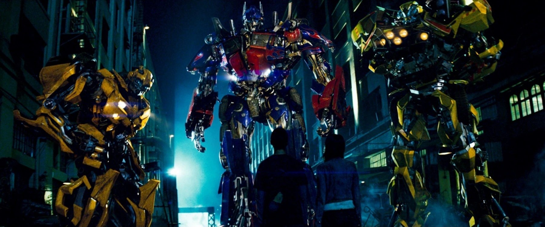 Un trío de robots gigantes parados frente a un hombre y una mujer jóvenes en un callejón oscuro en Transformers.