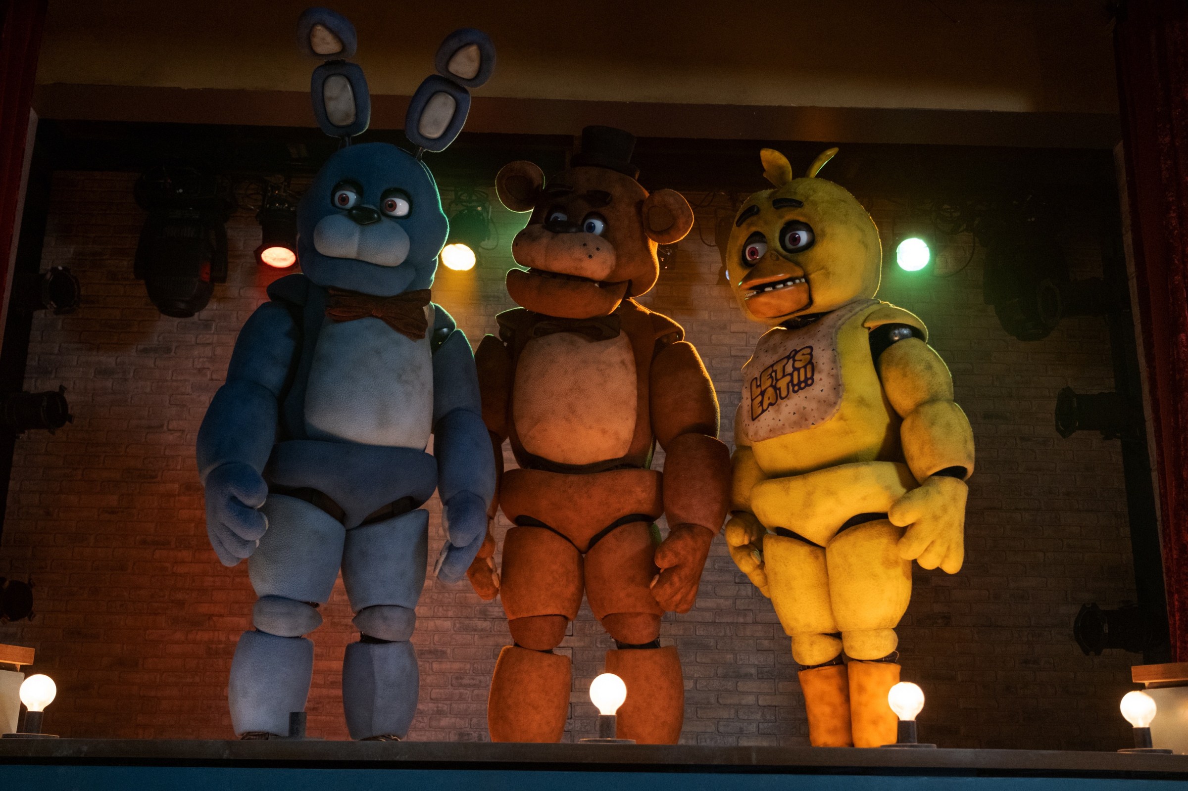 Animatronics Bonnie, Freddy Fazbear y Chica están en un escenario, mirando hacia la derecha, en la adaptación cinematográfica de Universal Pictures Five Nights at Freddy's.