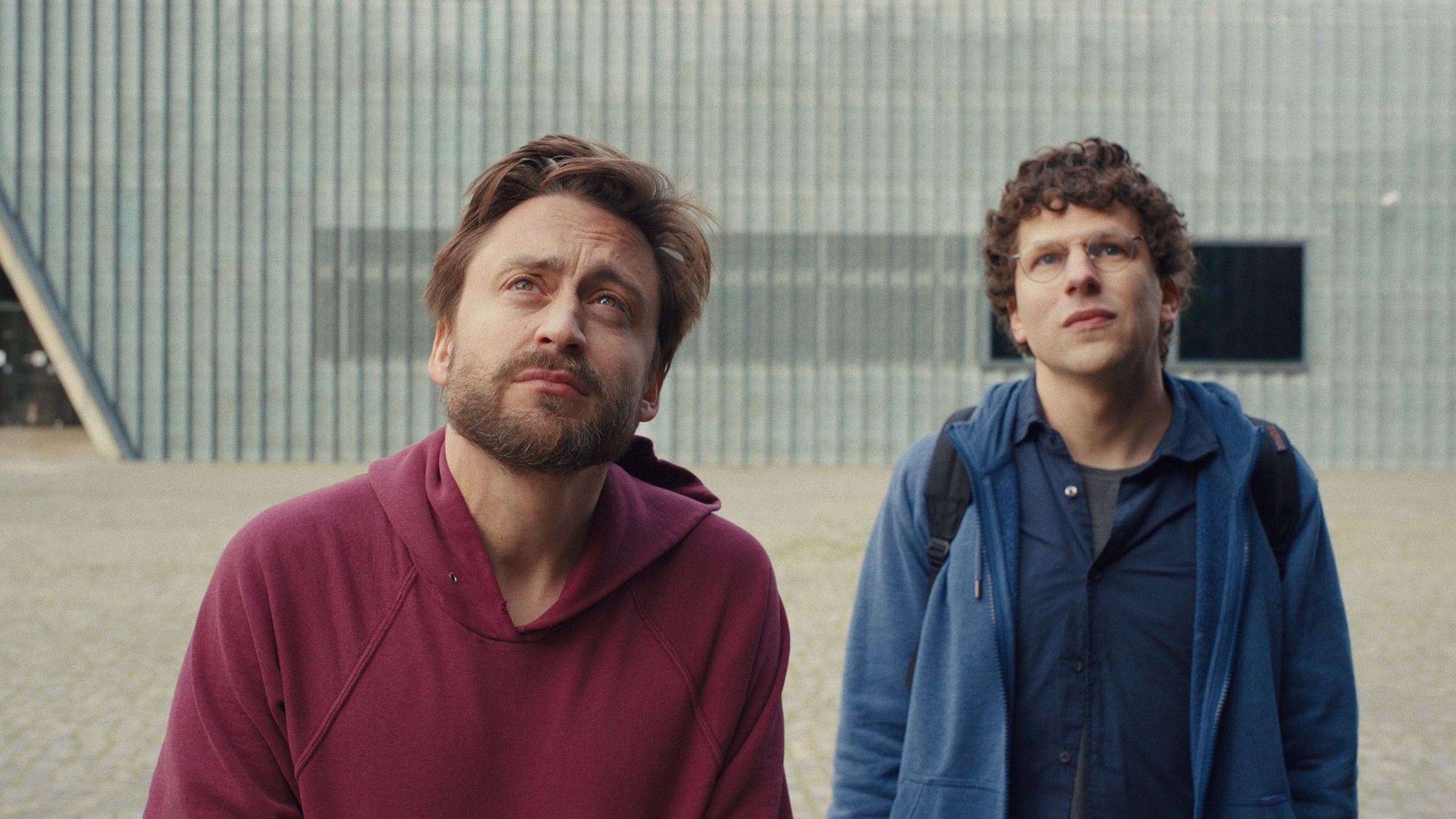Kieran Culkin y Jesse Eisenberg están afuera mirando algo en A Real Pain