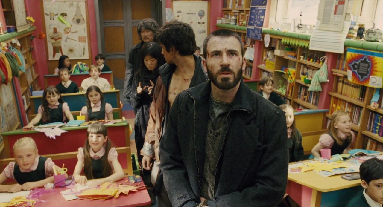 Chris Evans y un grupo de personas vestidas con ropa andrajosa de pie en un aula bien iluminada en Snowpiercer.