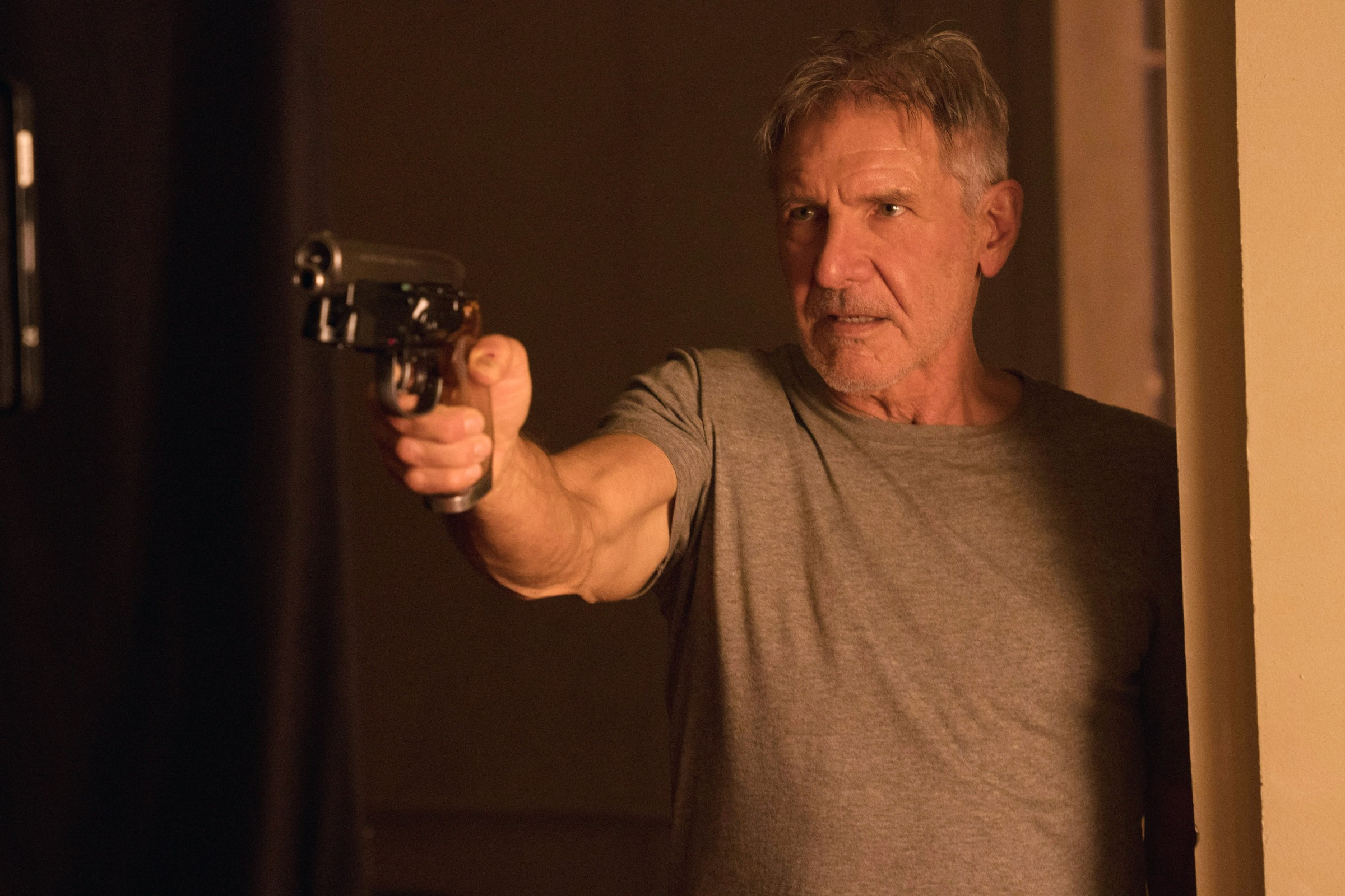 Harrison Ford de pie en una puerta sosteniendo una pistola futurista en Blade Runner 2049