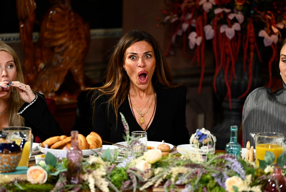 Una foto de los traidores de la temporada 3 que muestra a Dolores Catania luciendo extremadamente sorprendida sentada en una mesa de desayuno cubierta de vegetación, pasteles y jugo.
